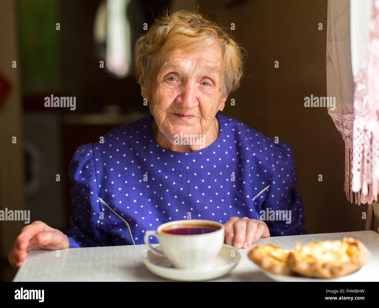Une femme âgée assise dans la cuisine à boire le thé. Banque D'Images