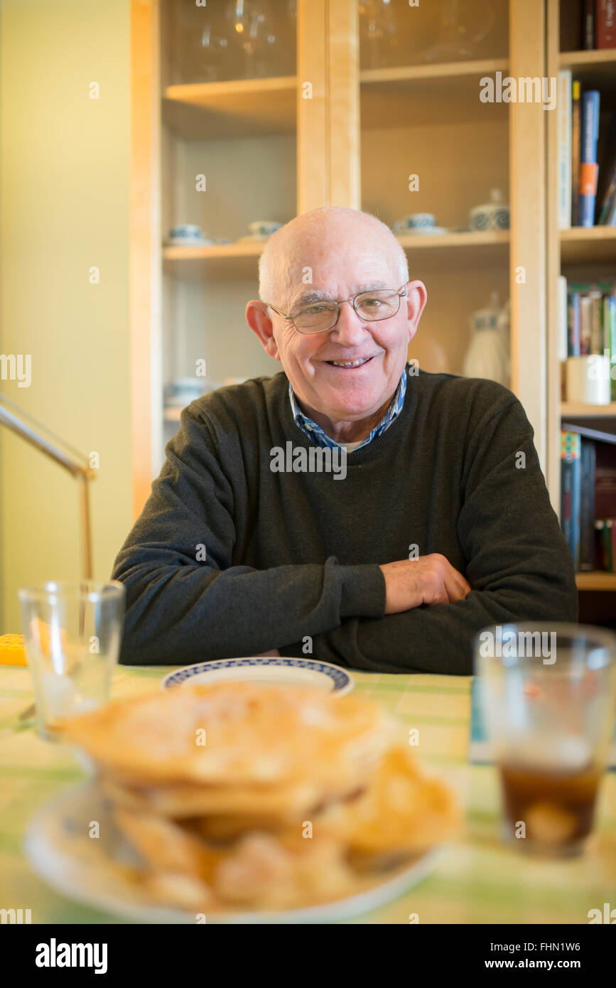 Portrait of smiling senior man sitting at table at home Banque D'Images