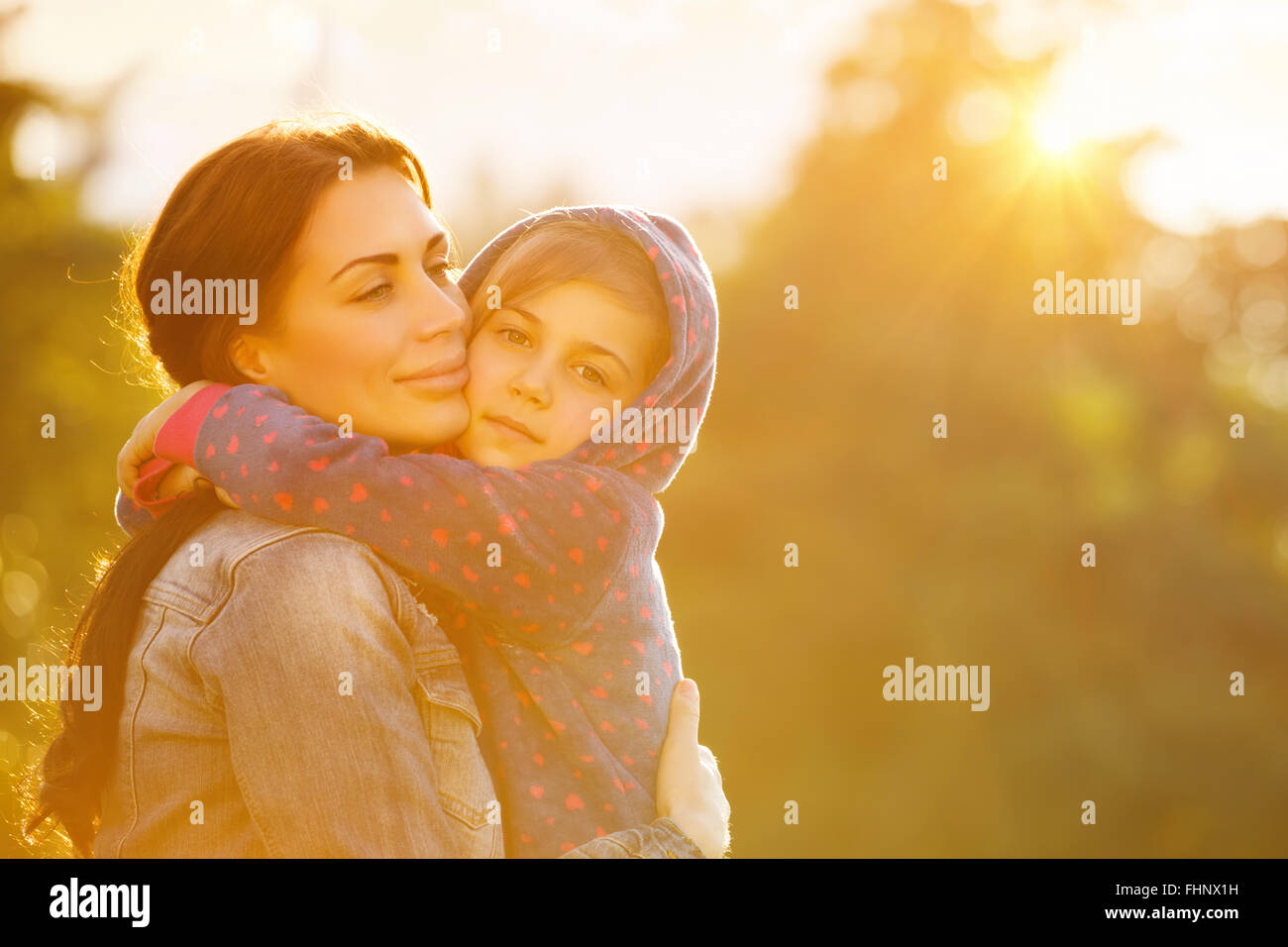 Portrait de belle mère avec amour serrant son précieux fille en jaune vif du soleil dans le parc, vie de famille heureuse Banque D'Images