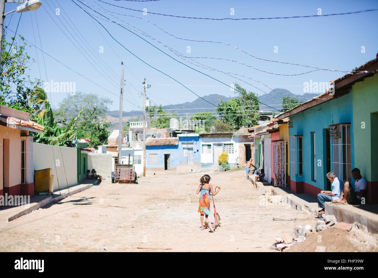 Dans un quartier pauvre de Trinidad à Cuba, une fille pousse son scooter en bas de la rue non pavée bordée de maisons aux couleurs Banque D'Images