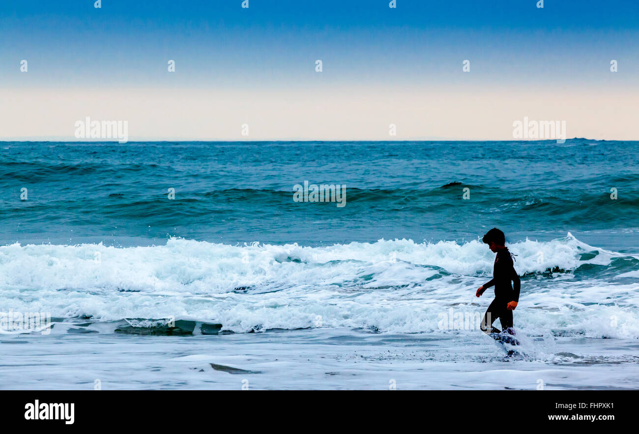 Silhouetté figure sur une plage avec des vagues se briser derrière Banque D'Images