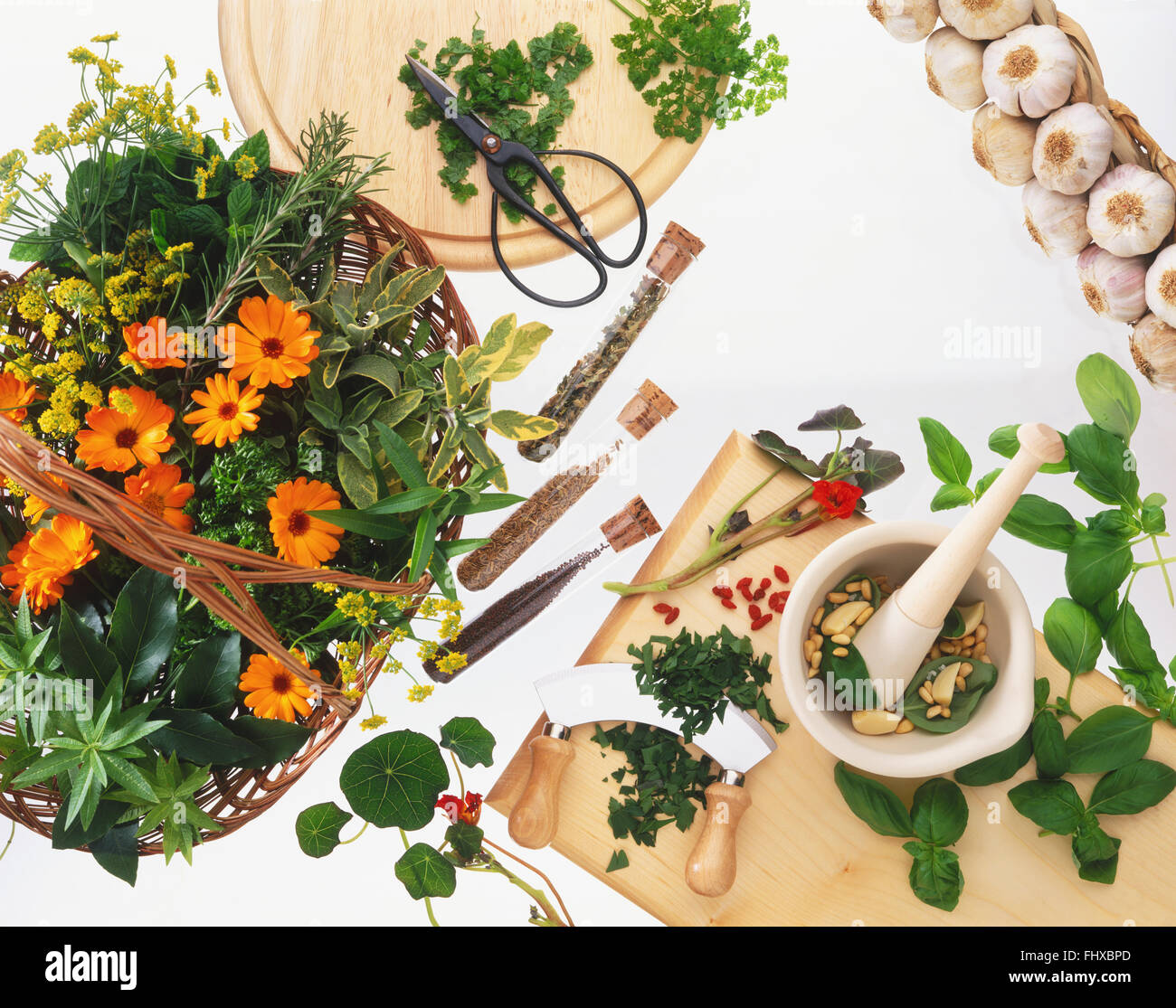 Fines herbes et fleurs dans un panier en osier, les herbes hachées sur une planche à découper, tubes à essai remplis de graines, mortier contenant des pignons de pin et basilic, les herbes et le poivre et une tresse d'ail Banque D'Images