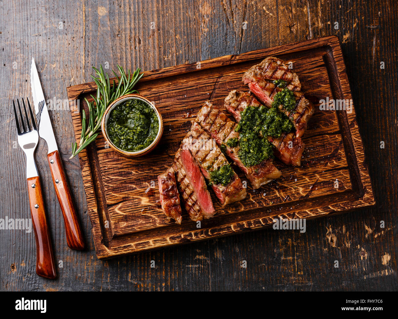 Meubles à point boeuf grillé steak de surlonge barbecue avec sauce Chimichurri sur une planche à découper sur fond sombre Banque D'Images