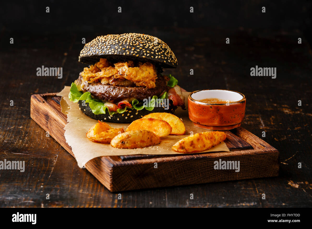 Burger noir avec graines de sésame oignon bacon viande frites joints toriques et les quartiers de pommes de terre sur fond de bois foncé Banque D'Images