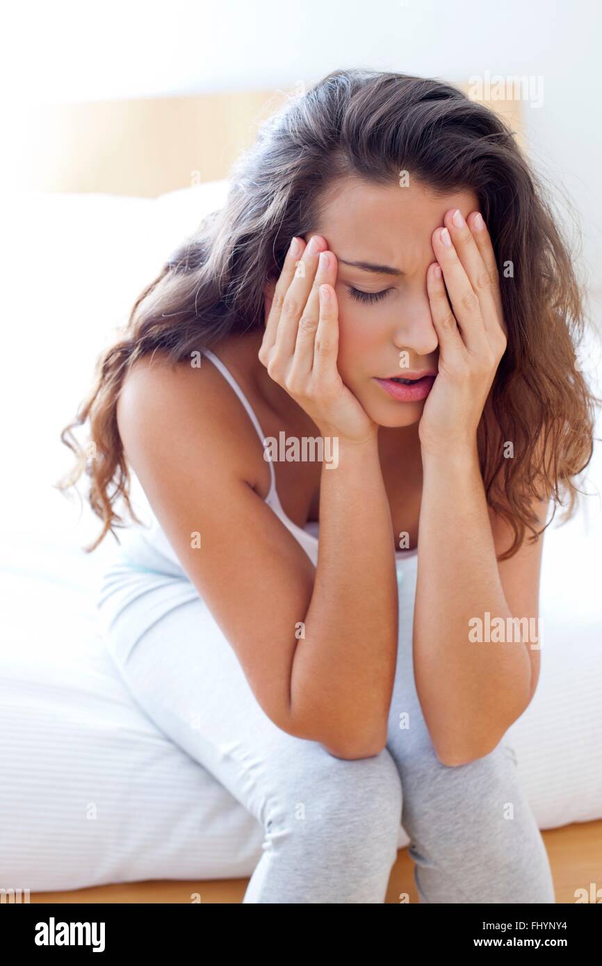 Parution du modèle. Femme assise sur son lit la tête et le visage de douleur. Banque D'Images