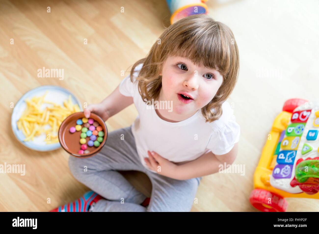 Parution du modèle. Jeune fille assise sur le sol avec un bol de bonbons, high angle view. Banque D'Images