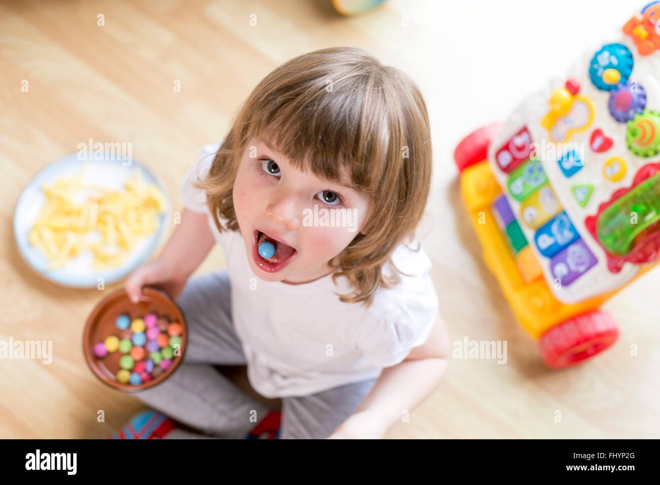 Parution du modèle. Jeune fille assise sur le sol avec un bol de bonbons, high angle view. Banque D'Images