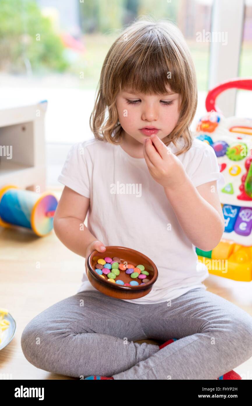 Parution du modèle. Jeune fille assise sur le sol avec un bol de bonbons. Banque D'Images