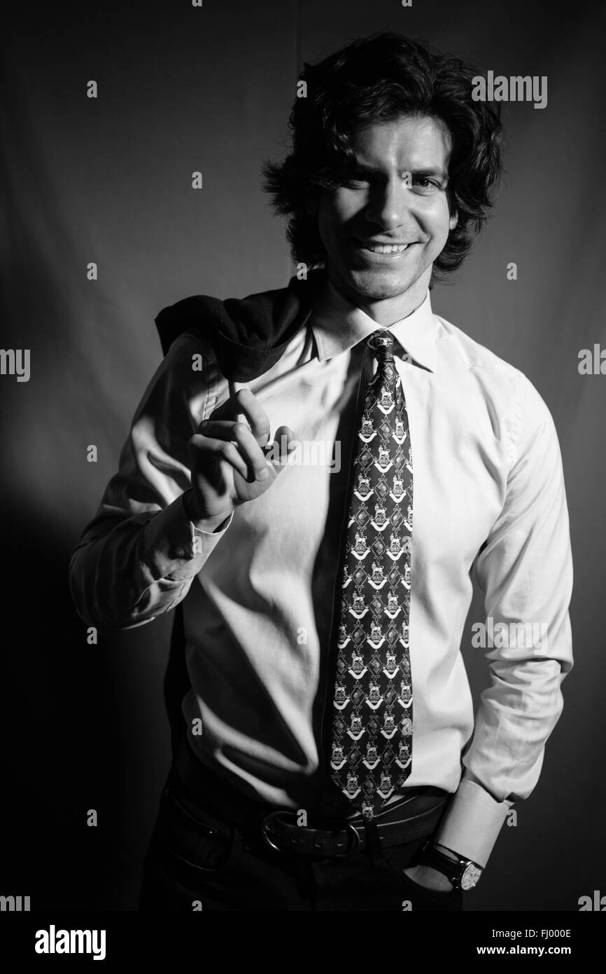 Jeune homme d'affaires dans une chemise avec une cravate de sourire et est titulaire d'une veste derrière le dos. Banque D'Images
