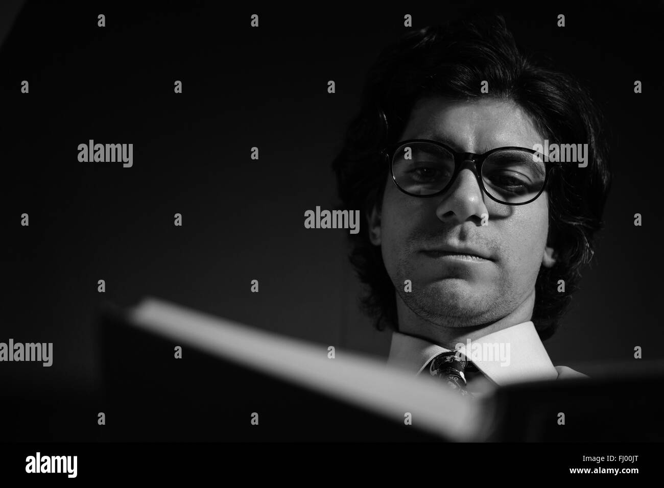 Homme lisant un livre avec des lunettes. Photo en noir et blanc d'une vue de bas en haut. Banque D'Images