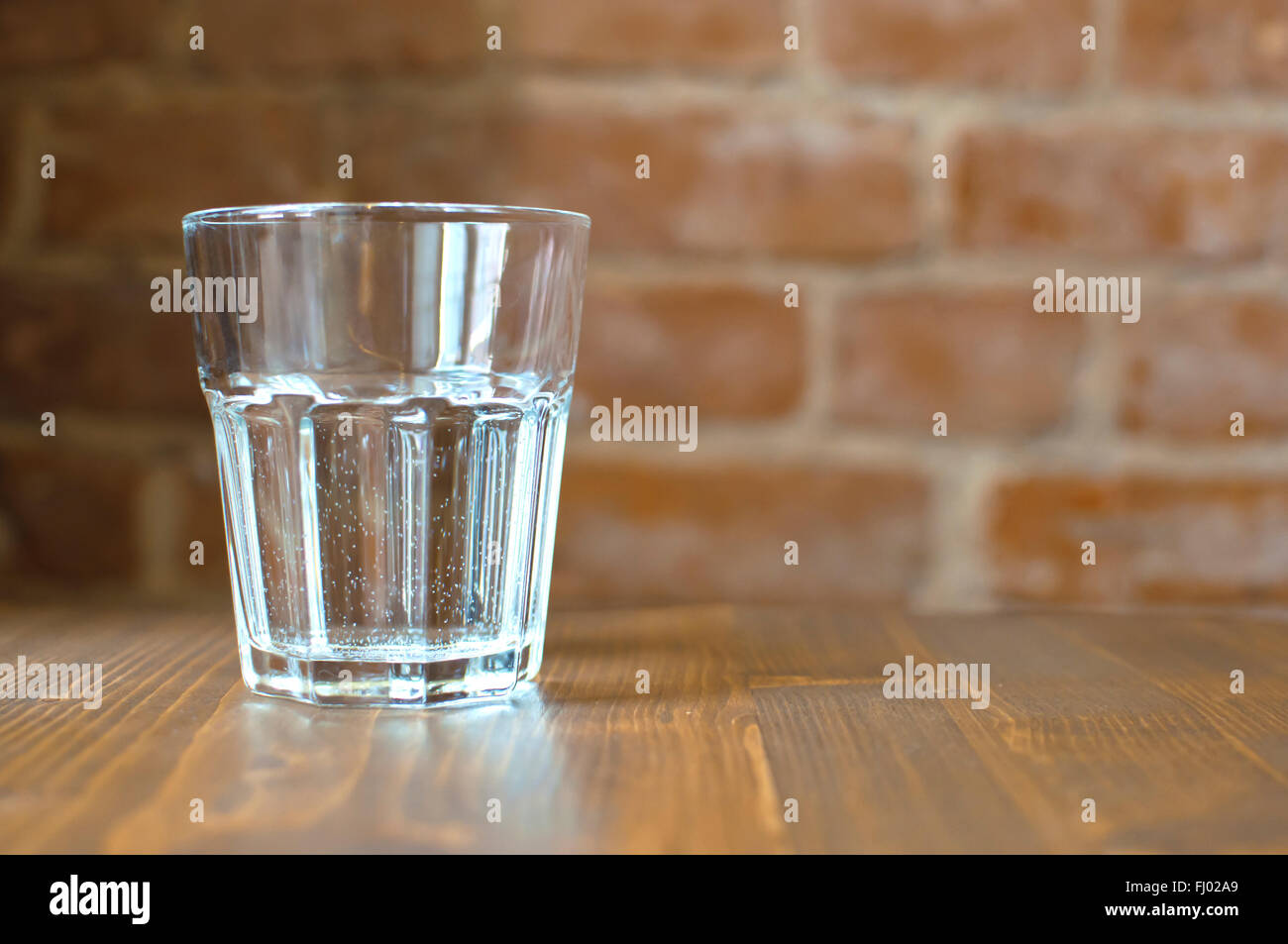 Verre d'eau sur une table en bois brun sur un fond de mur de briques rouges dans un café Banque D'Images