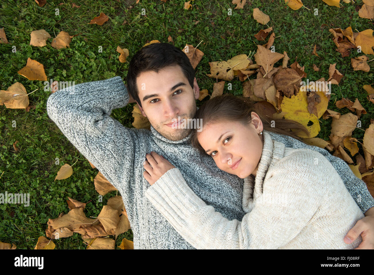 Jeune couple dans le parc, dans l'amour, allongé sur l'herbe verte et des feuilles jaunes Banque D'Images