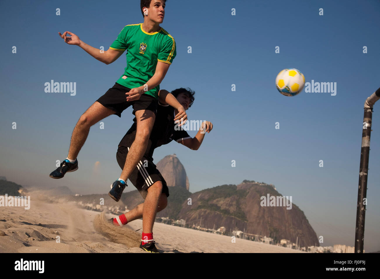 Les jeunes hommes jouent au football à la plage de Botafogo, à Rio de Janeiro, Brésil - mont du Pain de Sucre en arrière-plan. Banque D'Images