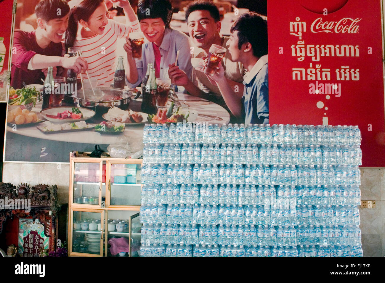 Les bouteilles en plastique sont empilés au-dessous d'un grand panneau publicitaire Coca Cola dans un restaurant à Skun, province de Kampong Cham, au Cambodge. Banque D'Images