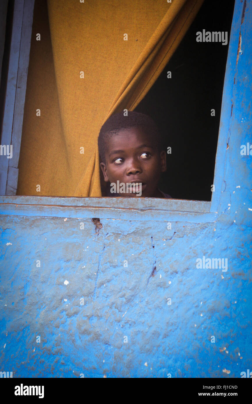 Enfant d'Afrique noire regarde à travers une fenêtre avec mur bleu à Jinka , Éthiopie Banque D'Images