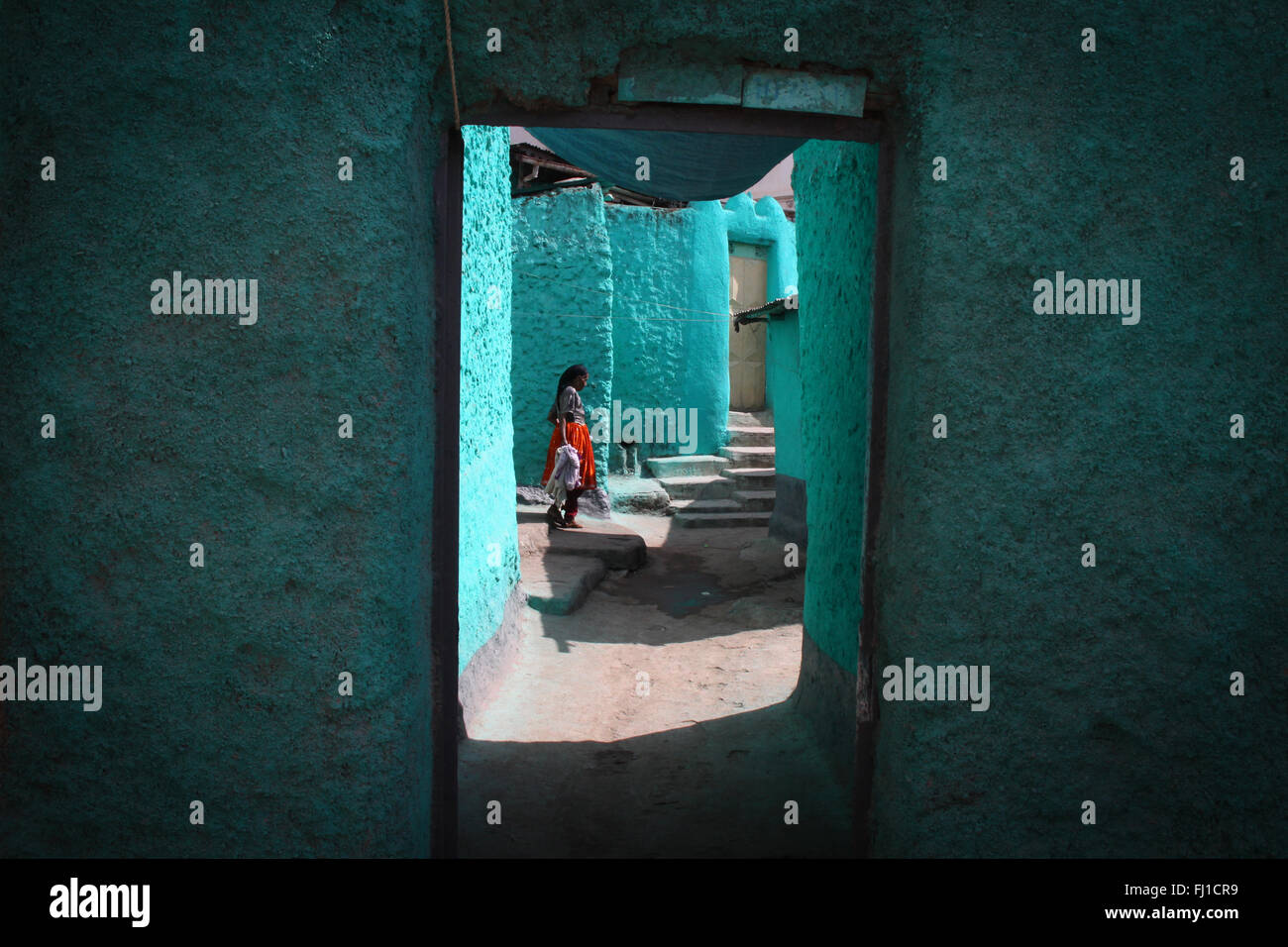 Une femme se tient dans la cour d'une maison traditionnelle turquoise bleu har, Harar, en Ethiopie Banque D'Images
