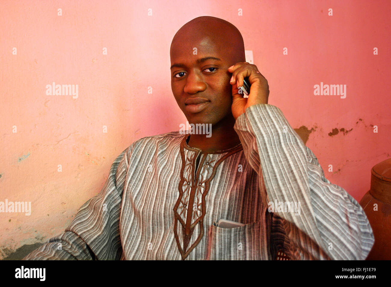 Portrait of handsome bald black homme africain du Mali avec un téléphone mobile de poser dans la ville de Djenné Banque D'Images