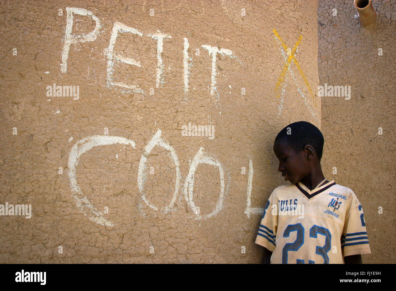 Enfant dans les rues de Djenné, Mali, avec 'PETIT COOL" écrit sur le mur ('Young et cool") Banque D'Images