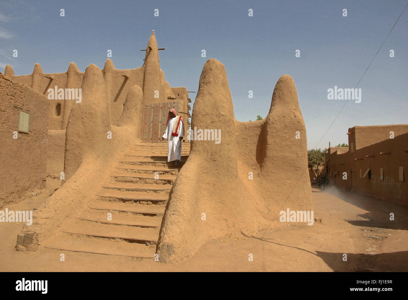 Un homme avec des vêtements traditionnels sort de la magnifique mosquée du banco de boue dans la région de Djenné, Mali, Afrique du Sud Banque D'Images