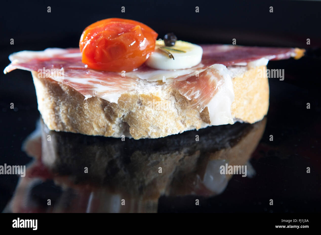 L'Espagnol tapa de jambon serrano servi sur des tranches de pain avec tomate et oeuf dur. Avec des réflexions isolées Banque D'Images