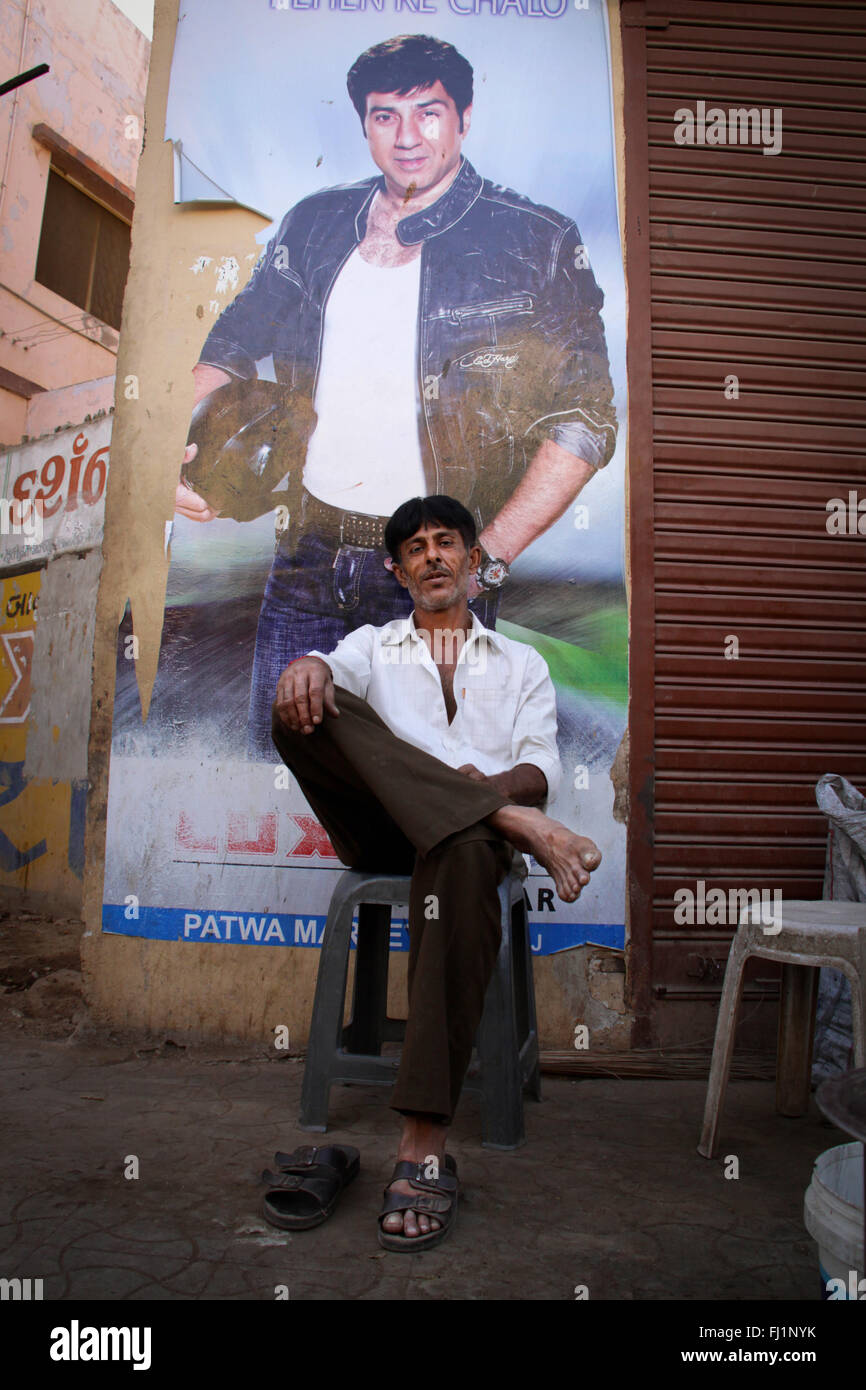 Homme assis seul dans une rue de Bhuj en face de Bollywood acteur immense poster , Gujarat, Inde Banque D'Images