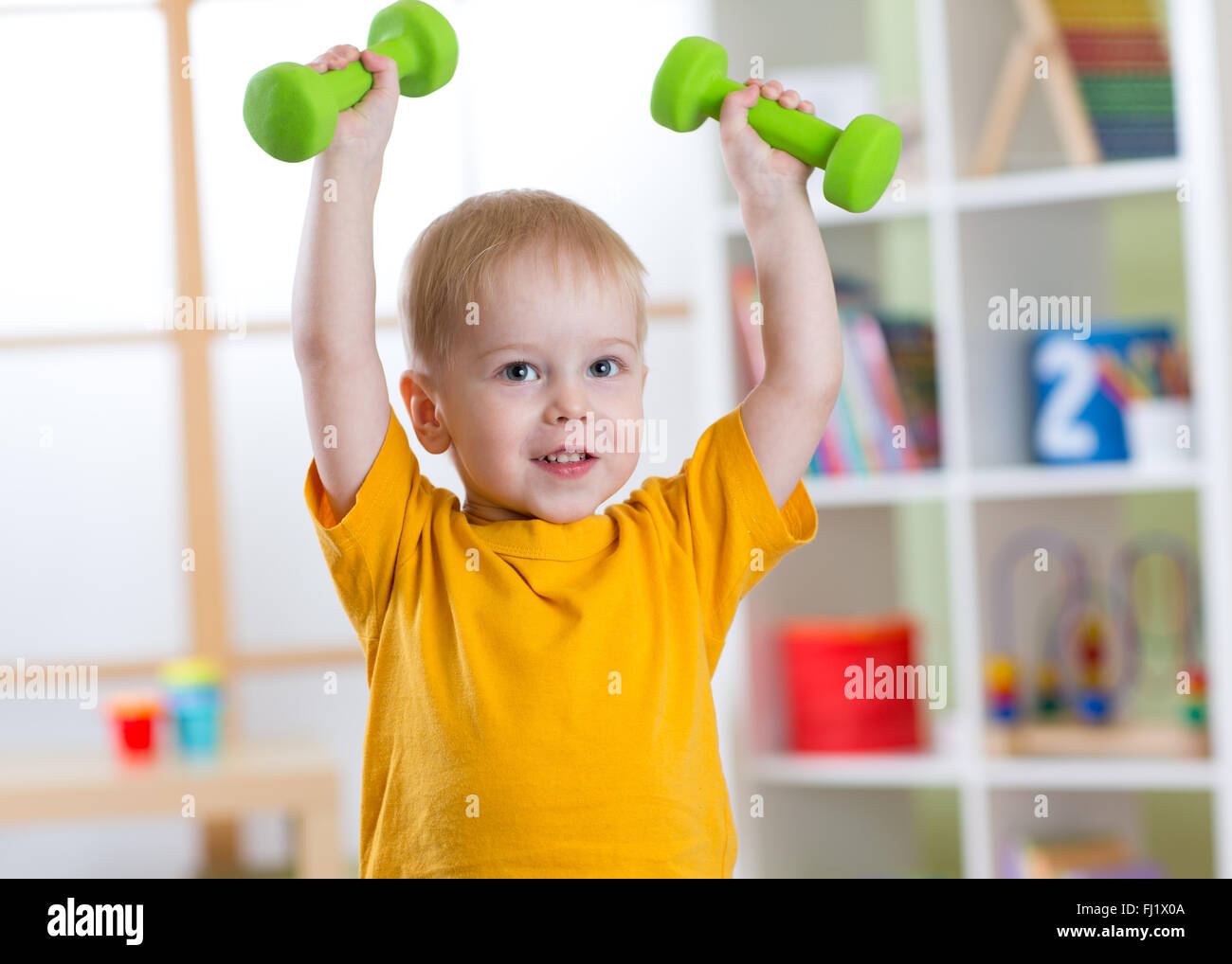 Smiling little boy exercising with dumbbells. La vie saine et du sport concept. Banque D'Images