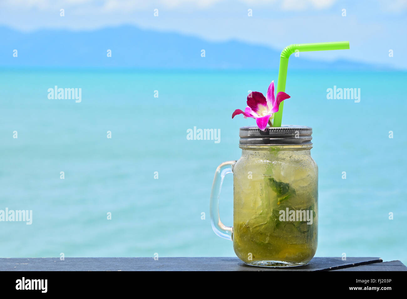 Gros bols style mug plein verre de mojito frais congelé avec capuchon métallique couvercle, paille et orchidée pourpre fleur en café sur la plage Banque D'Images