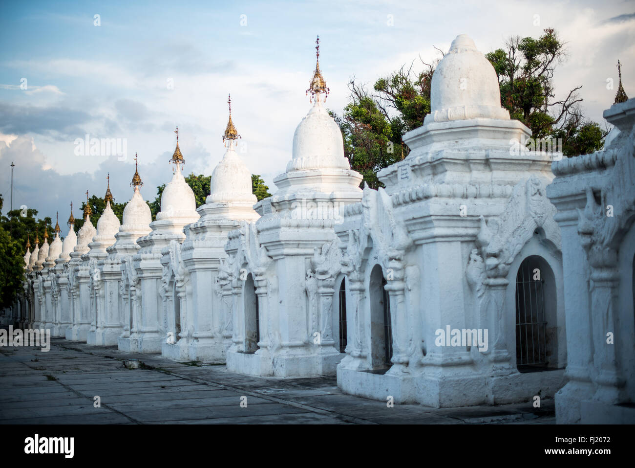 MANDALAY, Myanmar — des rangées de kyauksa gu (grottes avec inscription en pierre) blanches immaculées s'étendent sur les terres de la pagode Kuthodaw. Construit en 1857 par le roi Mindon, le complexe contient 729 dalles de marbre qui forment collectivement ce que l'on appelle le plus grand livre du monde. Chaque petit stupa abrite une tablette de marbre gravée sur les deux faces avec le texte du Tipitaka, le canon Pali complet du bouddhisme Theravada. La disposition ordonnée de ces structures reflète les principes architecturaux bouddhistes traditionnels. Banque D'Images