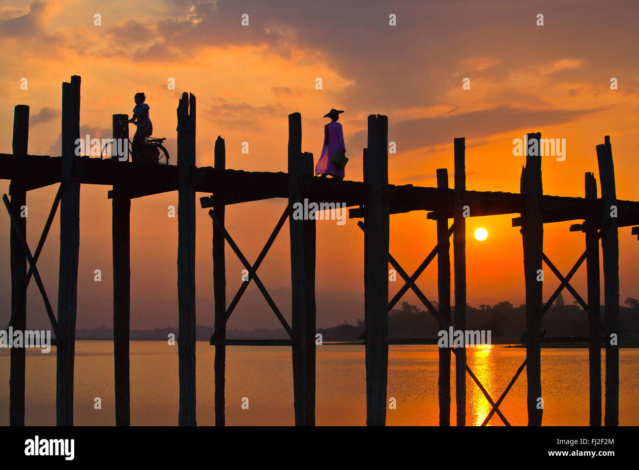 Les Birmans utilisent le pont en teck U BEINS de commuer à travers le lac Taungthaman au lever du soleil - AMARAPURA, MYANMAR Banque D'Images