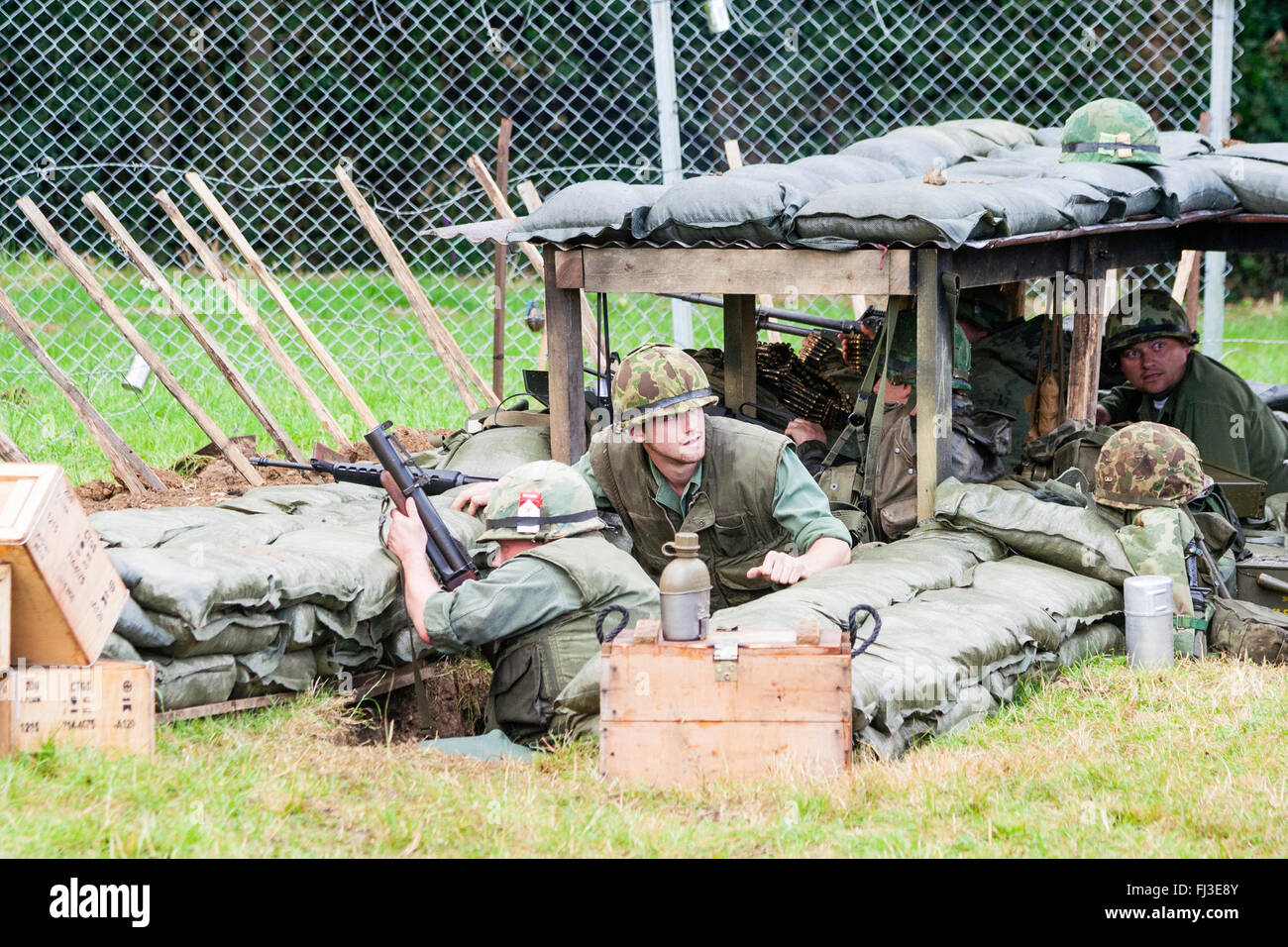 La guerre et la paix, l'Angleterre. Reconstitution de la guerre du Vietnam. Base de feu américain attaqué par ennemi invisible dans les bois, les soldats derrière le fil de feu. retour Banque D'Images