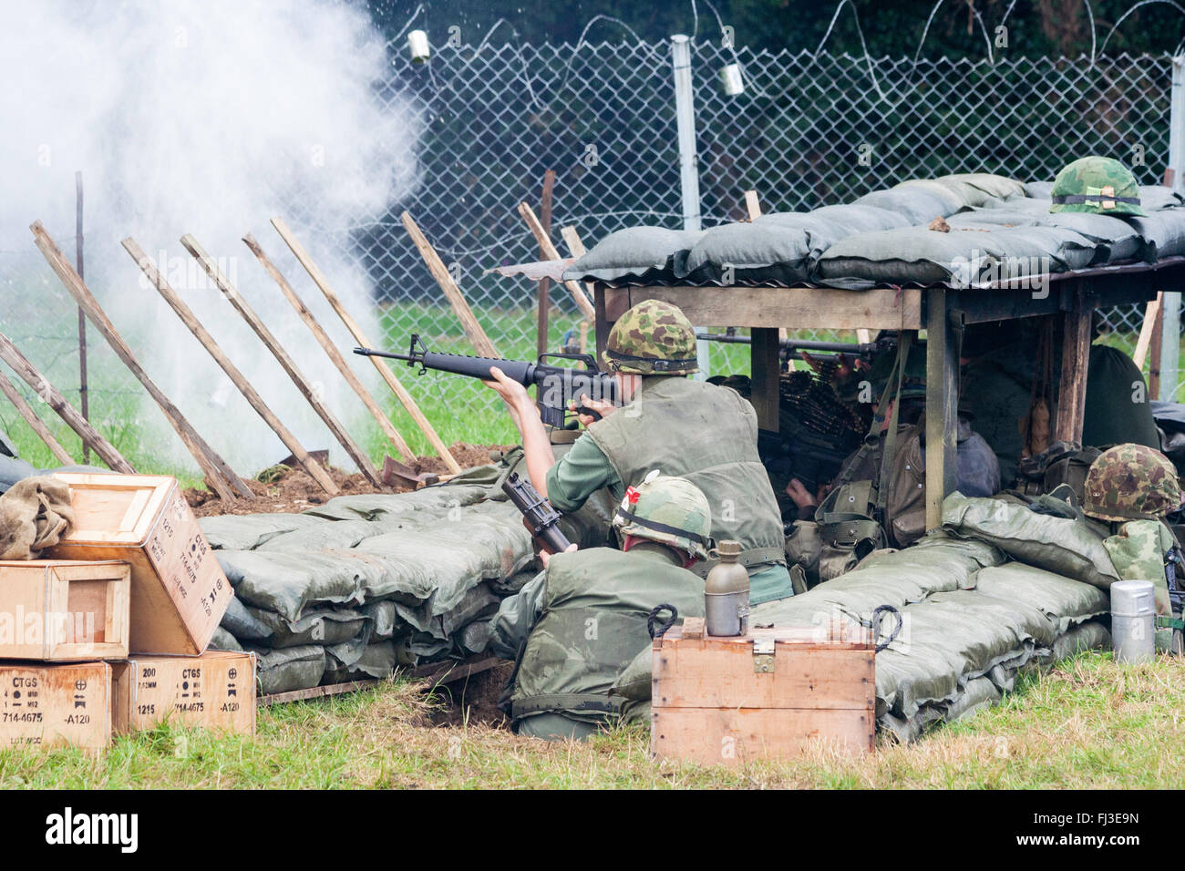 La guerre et la paix, l'Angleterre. Reconstitution de la guerre du Vietnam. Base de feu américain attaqué par ennemi invisible dans les bois, les soldats derrière le fil de feu. retour Banque D'Images