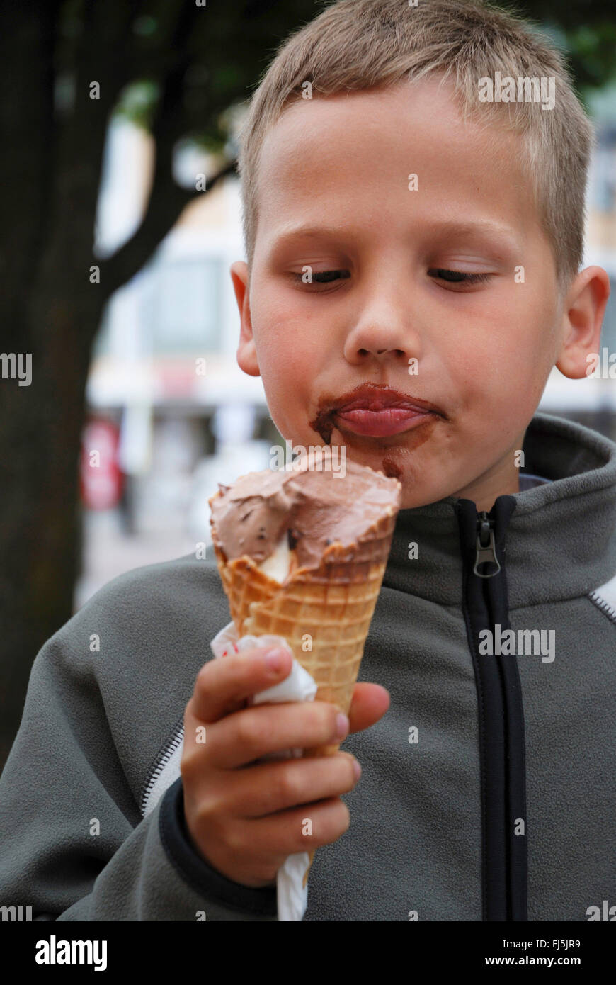 Petit garçon avec des traînées de manger avec plaisir un visage crème glacée au chocolat, portrait d'un enfant, Allemagne Banque D'Images