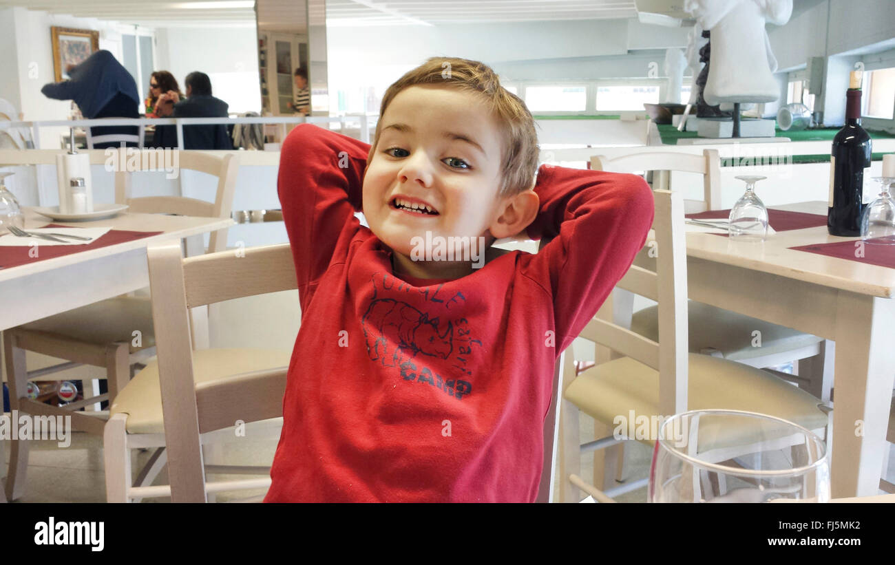 Heureux petit garçon assis à un bureau dans un restaurant, Allemagne Banque D'Images