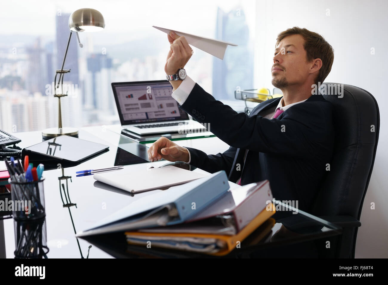 Gestionnaire d'entreprise dans un bureau moderne prend une pause et prépare un avion en papier. L'homme s'ennuie rêve de ses prochaines vacances Banque D'Images