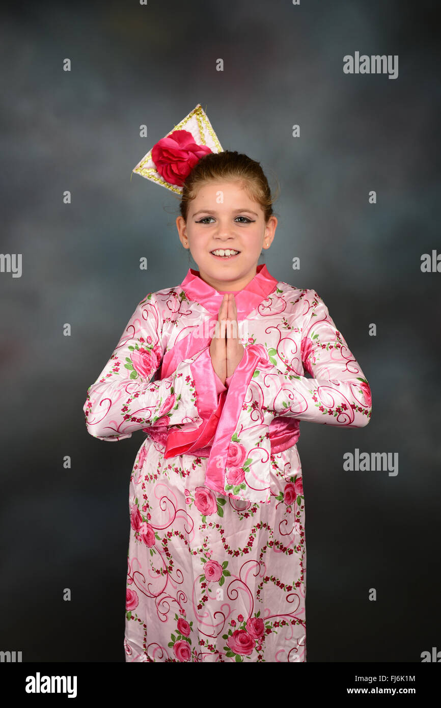 Adorable jeune fille déguisée en Geisha contre fond gris. Banque D'Images