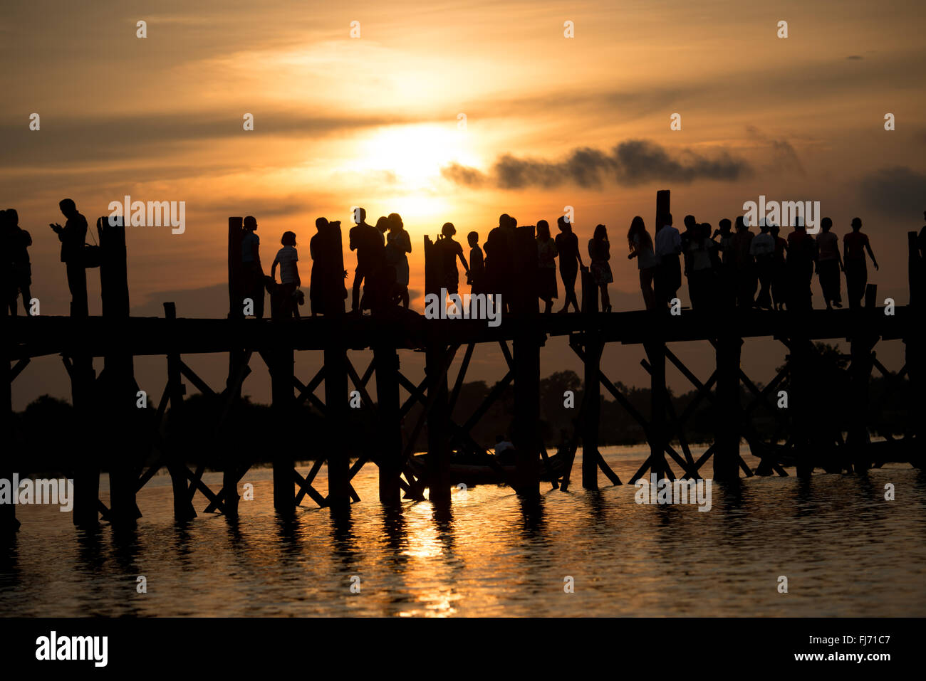 AMARAPURA, Myanmar — le pont U Bein s'étend sur le lac Taungthaman près de Mandalay. La structure en teck de 1,2 kilomètres de long, considérée comme le plus ancien et le plus long pont en teck du monde, est silhouette sur le ciel. Les piétons et les moines locaux traversent le pont pendant que les touristes observent la scène emblématique, particulièrement populaire au coucher du soleil. Banque D'Images