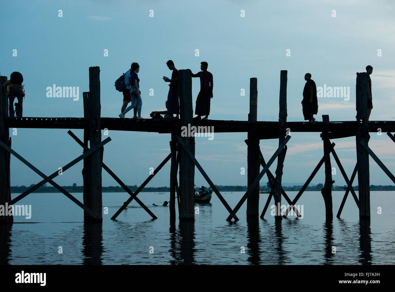 AMARAPURA, Myanmar — le pont U Bein s'étend sur le lac Taungthaman près de Mandalay. La structure en teck de 1,2 kilomètres de long, considérée comme le plus ancien et le plus long pont en teck du monde, est silhouette sur le ciel. Les piétons et les moines locaux traversent le pont pendant que les touristes observent la scène emblématique, particulièrement populaire au coucher du soleil. Banque D'Images