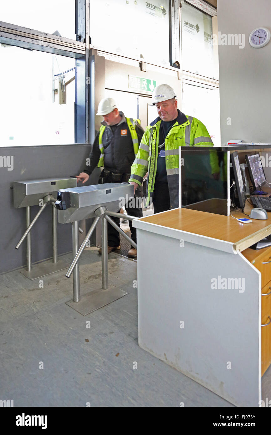 Deux travailleurs entrer dans un chantier de construction à l'aide d'un tourniquet de sécurité activé par un lecteur d'empreintes digitales Banque D'Images