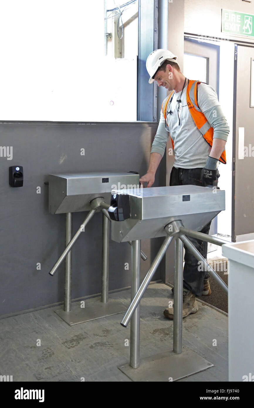 Un travailleur entre dans un site de construction à l'aide d'un tourniquet de sécurité activé par un lecteur d'empreintes digitales Banque D'Images
