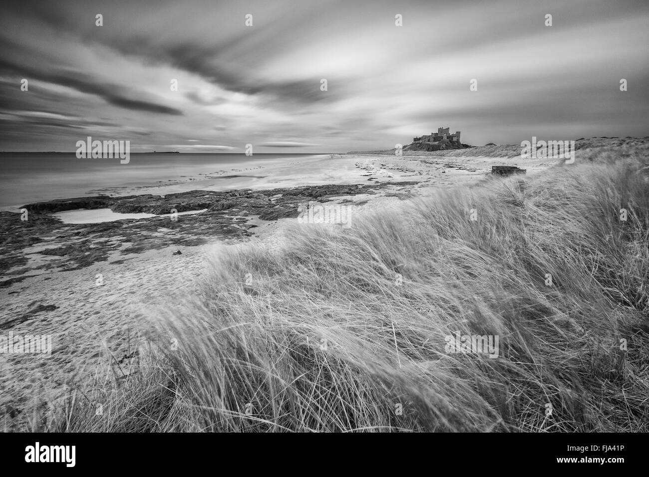 Château de Bamburgh des dunes vers le nord. Une longue exposition a admis les nuages et l'herbe à blur Banque D'Images