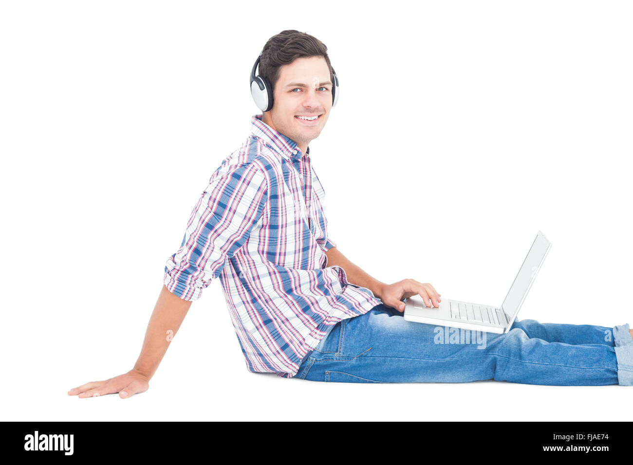 Écouteurs avec l'homme assis sur le plancher à l'aide d'ordinateur portable Banque D'Images