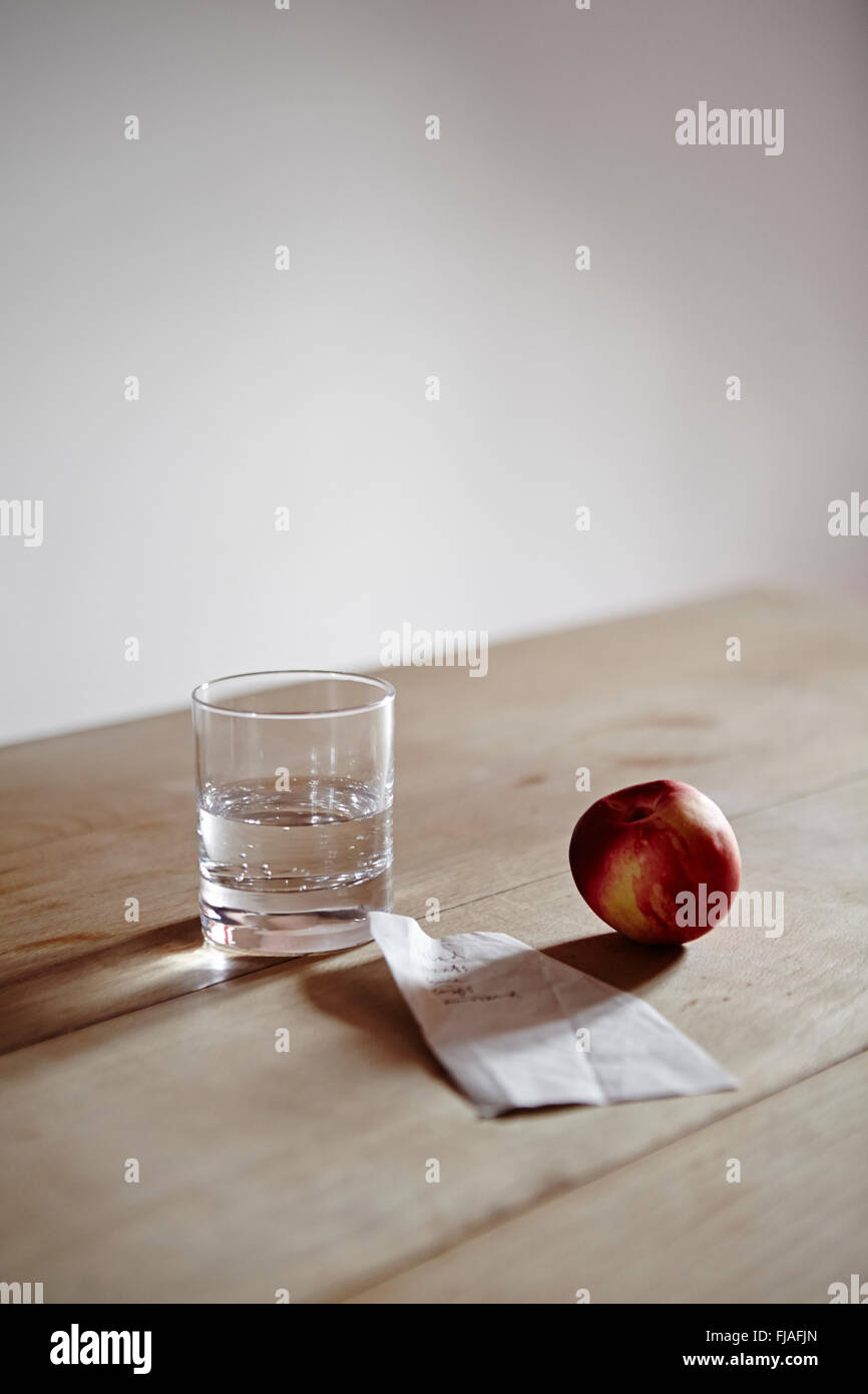 Un verre d'eau, une nectarine et une liste de courses sur la table de la cuisine. Banque D'Images