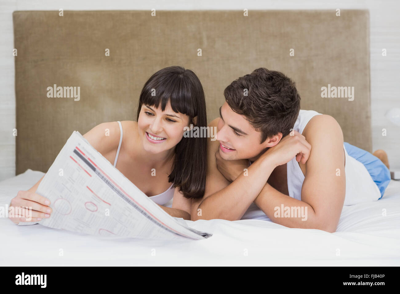 Couple reading newspaper on bed Banque D'Images