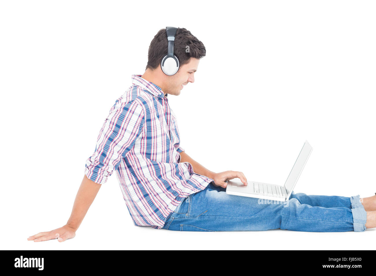 Écouteurs avec l'homme assis sur le plancher à l'aide d'ordinateur portable Banque D'Images
