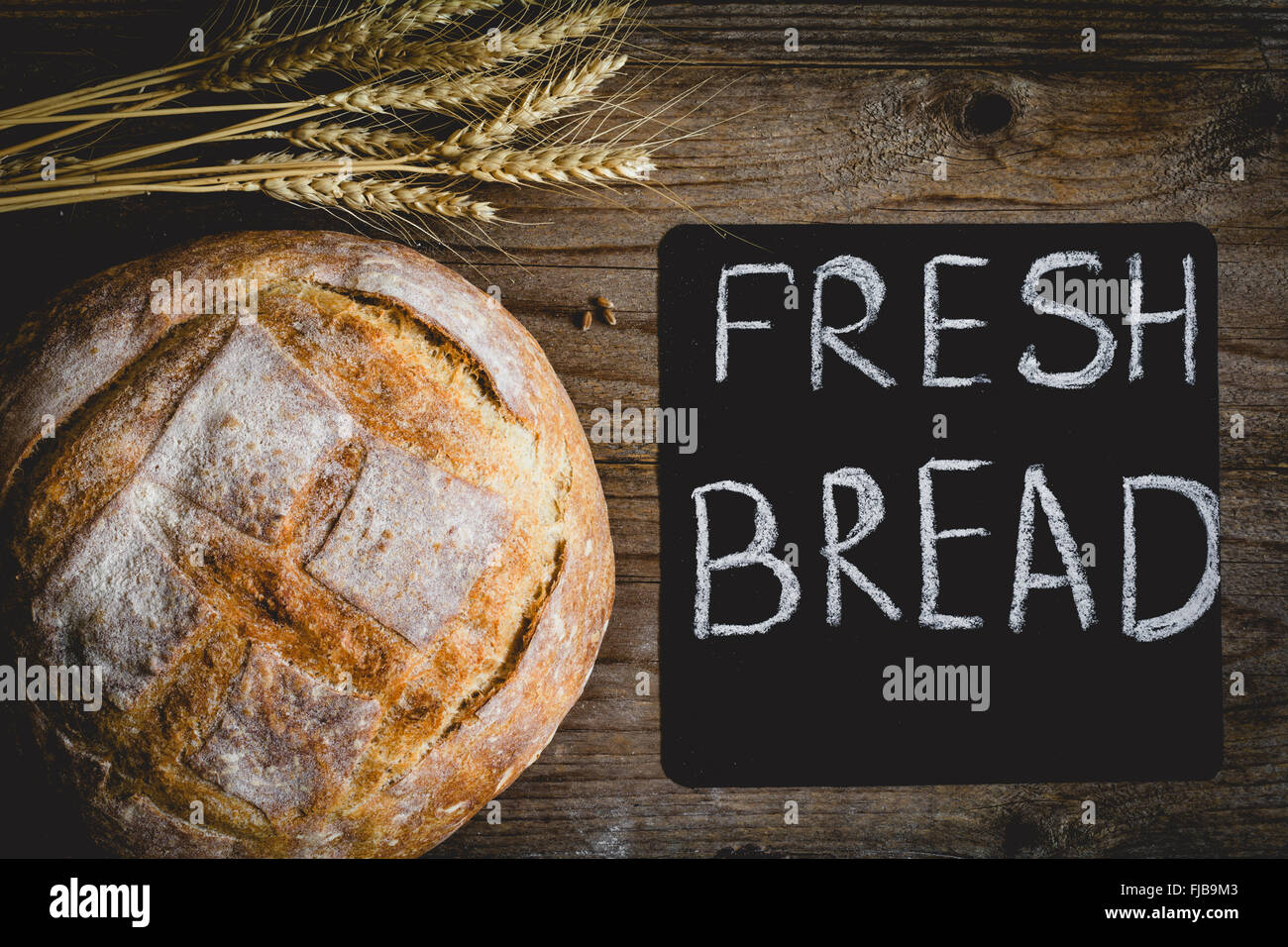 Round miche de pain, du pain au levain sur fond de bois. Tableau et tas de blé tendre les ressorts de l'oreille sur le côté Banque D'Images