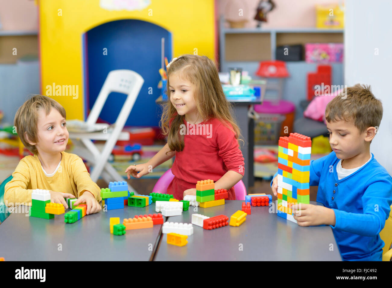 Trois enfants heureux de jouer avec des blocs de construction en plastique à l'école maternelle Banque D'Images
