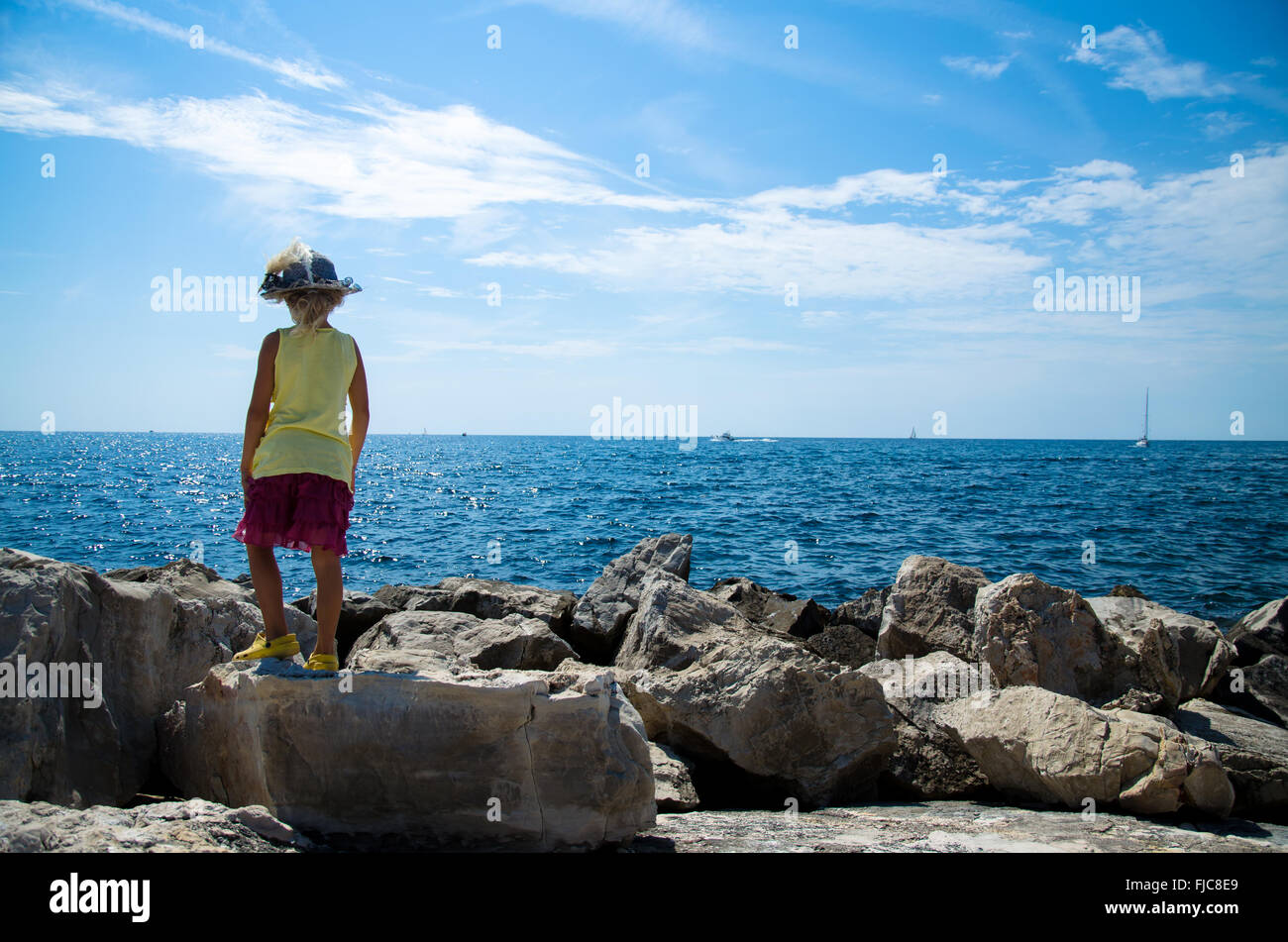 Petite fille debout sur le rocher observant la mer bleue Banque D'Images