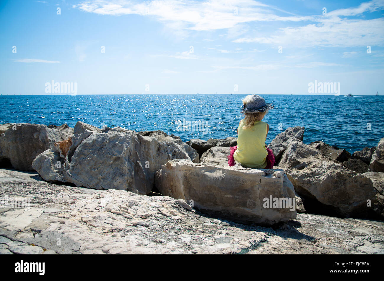 Petite fille assise dans l'observation de la mer bleu rock Banque D'Images