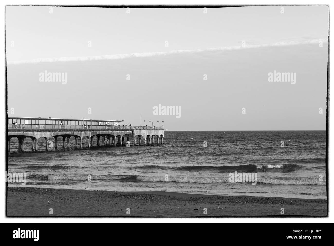 Une image en noir et blanc de la lumière au coucher du soleil d'un pilier à la direction de la mer à la plage de sable et une bande de nuages dans le Banque D'Images