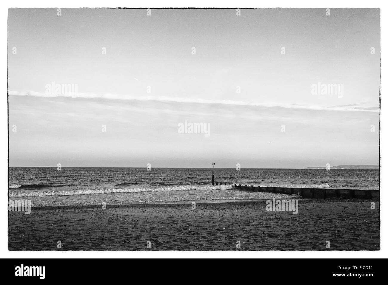 Une image en noir et blanc de la lumière au coucher du soleil d'un pilier à la direction de la mer à la plage de sable et une bande de nuages dans le Banque D'Images